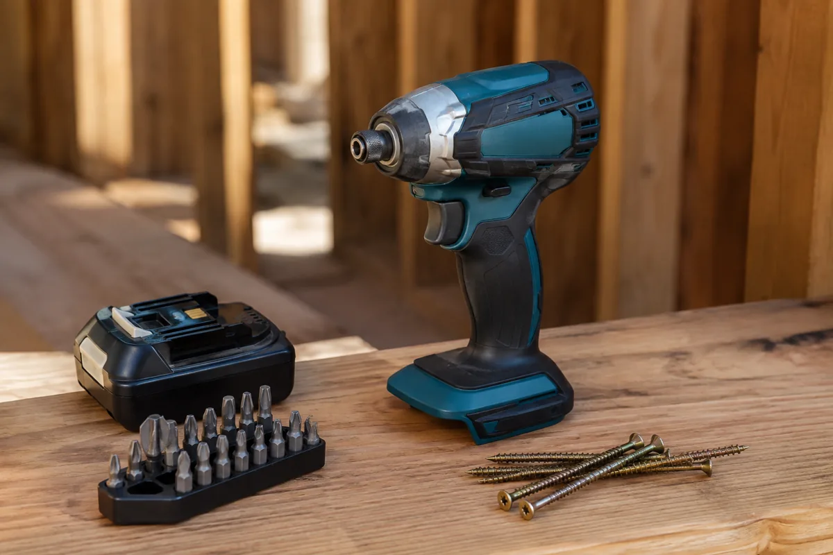 Cordless impact driver with a hex collet beside a battery, driver bits and deck screws